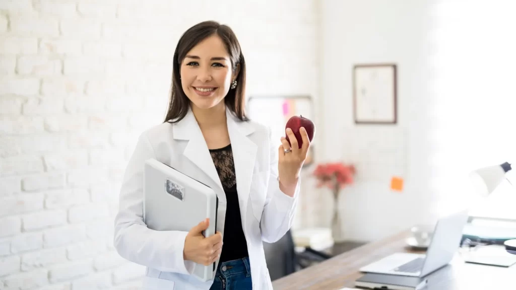 Smiling dietitian holding an apple and a laptop, reflecting a passion for nutrition and well-being - Is Dietetics for You?