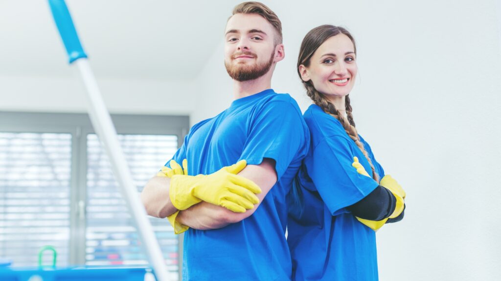 Two janitors in blue uniforms with cleaning gloves standing back to back