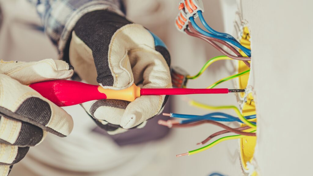 Electrician using a screwdriver to connect wires, illustrating when to call a professional for electrical issues