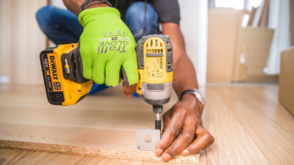 Handyman using a cordless drill to assemble furniture, showcasing an essential handyman tool list item