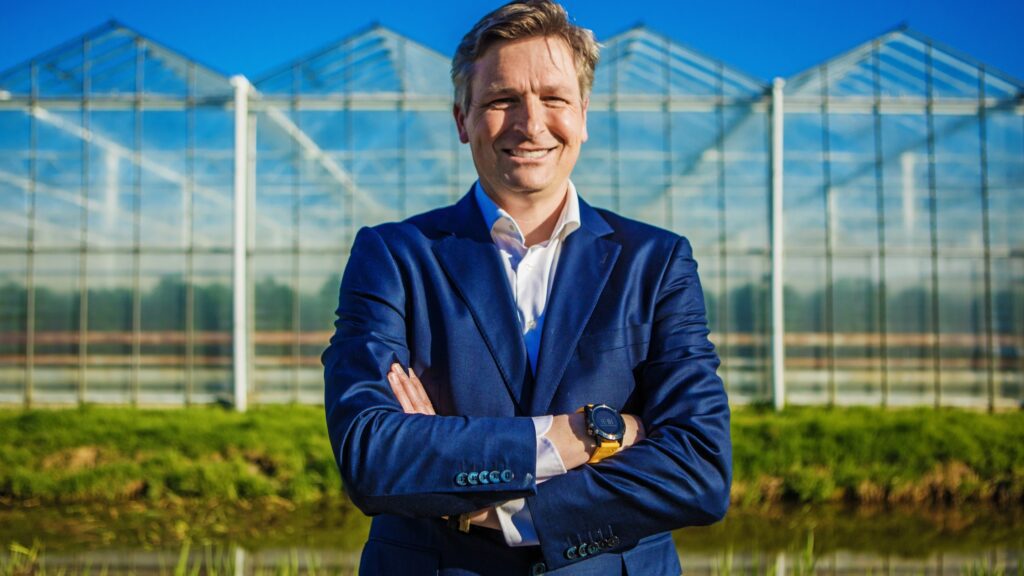 Greenhouse manager smiling in front of a greenhouse, reflecting the rewarding career and salary potential in this field