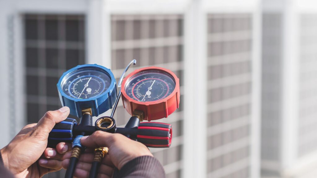 HVAC technician using manifold gauge set to measure refrigerant pressure, essential in HVAC technician tool list