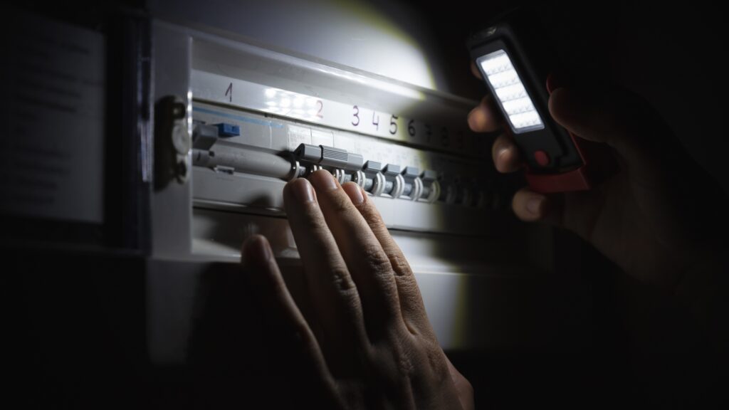 Inspecting an electrical breaker after a power surge, showing how power surges happen in homes due to overloaded circuits