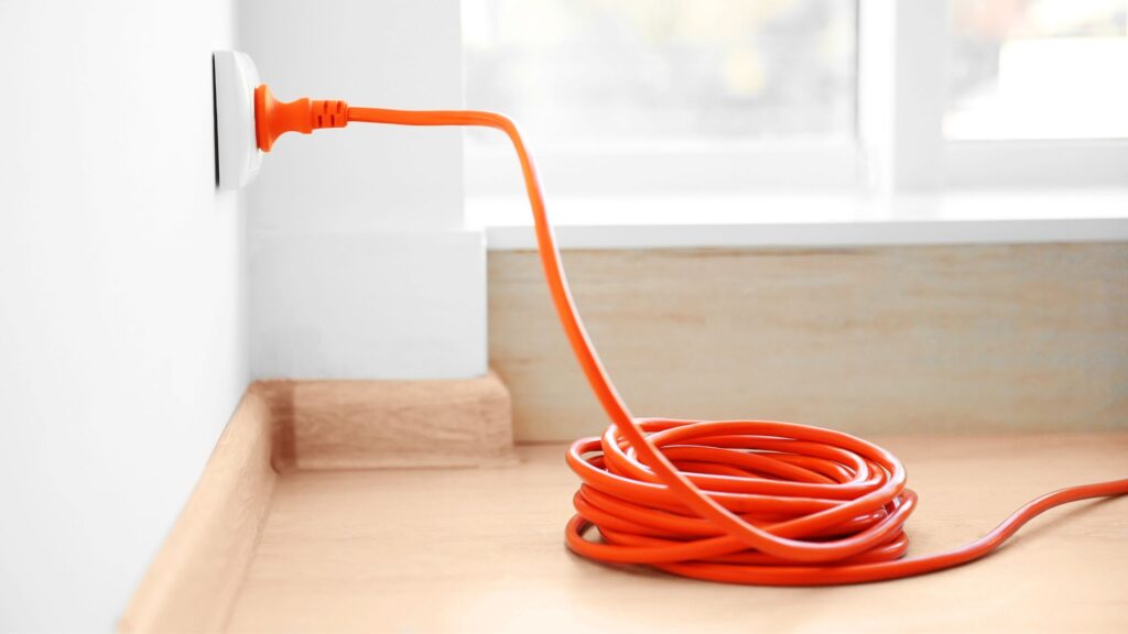 Coiled orange extension cord plugged into a wall, emphasizing the importance of proper storage when choosing the right extension cord