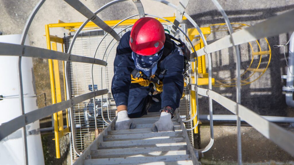 Worker climbing an industrial ladder with safety gear, showing the importance of choosing the right ladder for trades