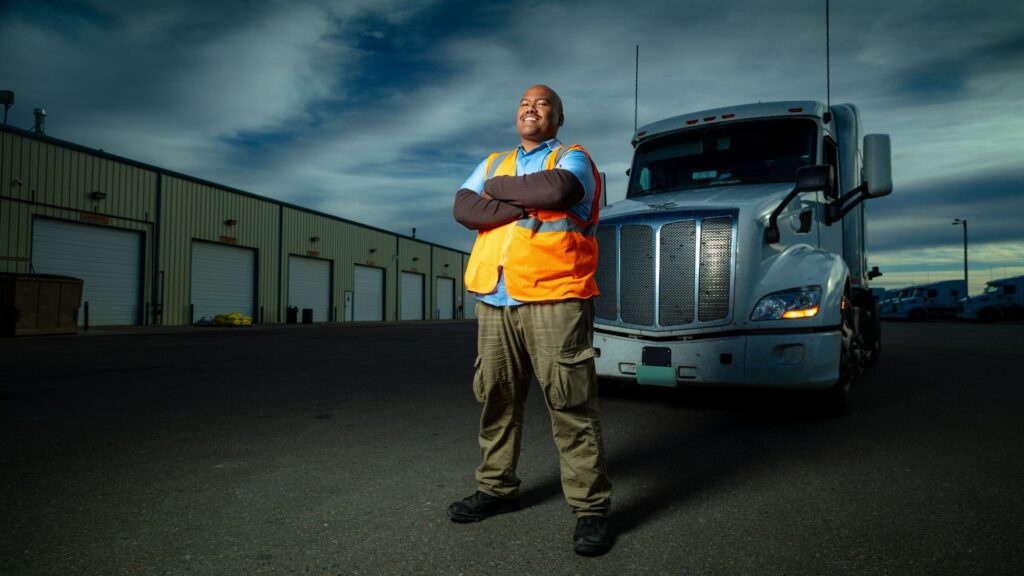 Truck driver in durable work clothes and safety boots, standing confidently by the truck, ready for all-weather conditions